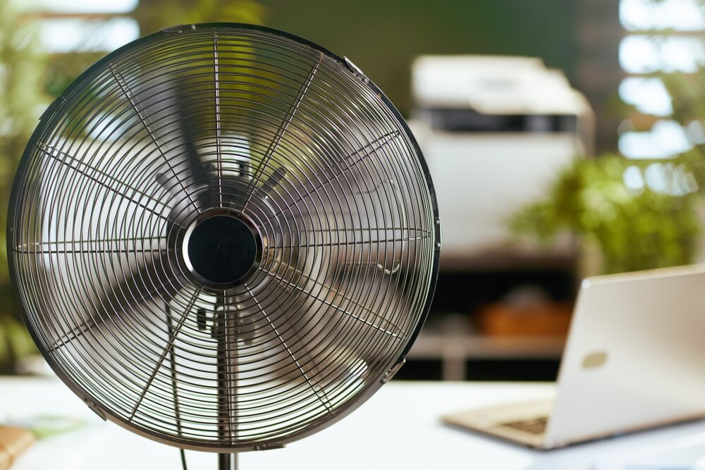 Electric fan blowing warm air in modern interior, showing limited effectiveness without portable air con in enclosed spaces